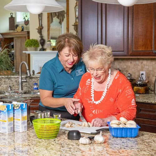 A female Right at Home caregiver is helping her senior female client cut vegetables in the kitchen 