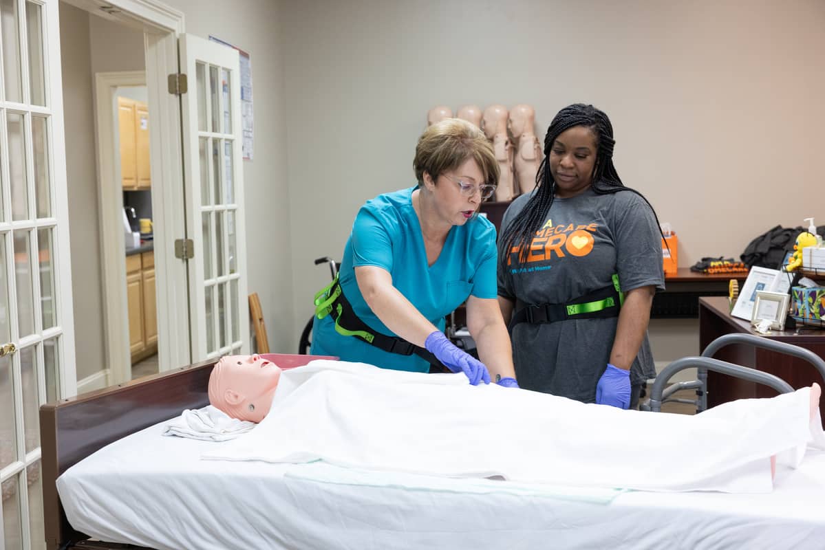 Female Right at Home caregiver training a new female caregiver using a test dummy