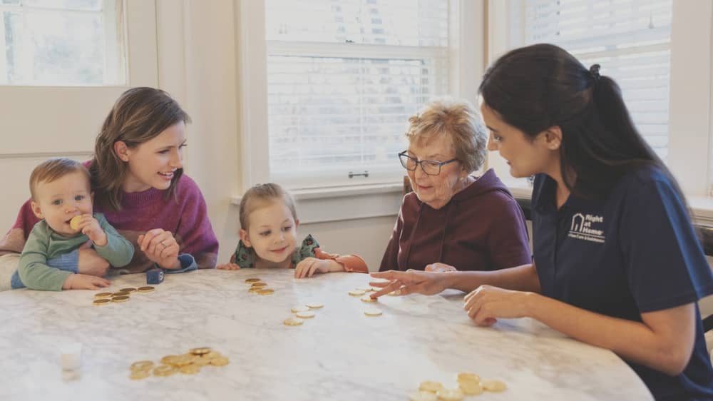 Right at Home caregiver sitting with a family at a table and playing a game for Hanukkah
