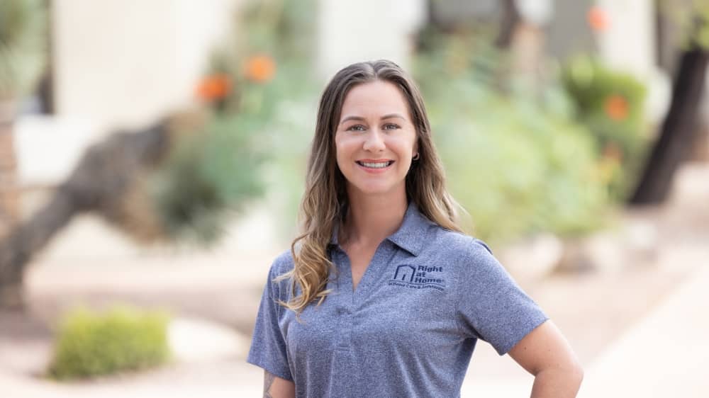 Woman smiling at the camera wearing a grey Right at Home t-shirt against an outdoor background