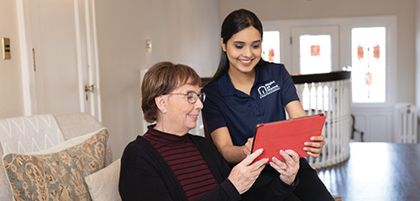 Female Right at Home caregiver smiling at a table with a female senior client