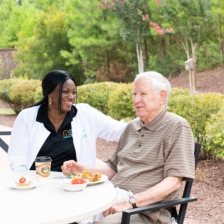 Caregiver smiling with a male senior client at an outdoor patio table