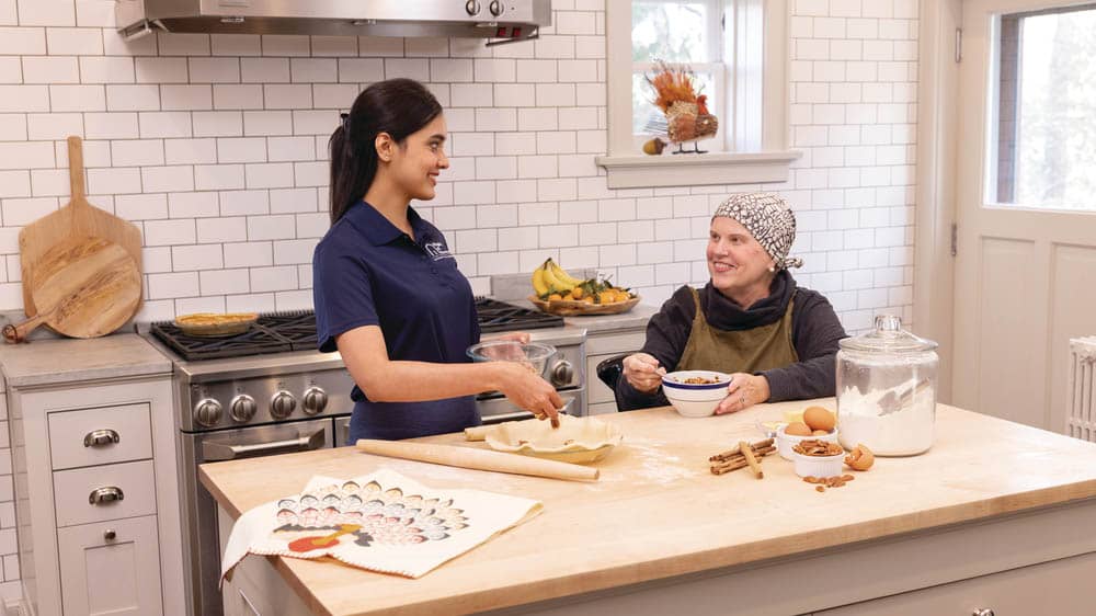 A female Right at Home caregiver is helping a senior female client make a pie in a kitchen