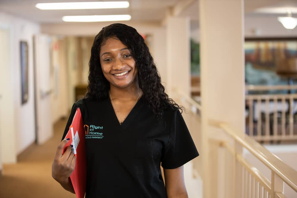 Female Right at Home caregiver standing in a hallway holding a folder
