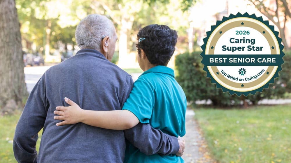 Female Right at Home caregiver helping a senior male client walk outside with a Caring.com 2026 Caring Super Star Award Badge in the upper right hand corner.