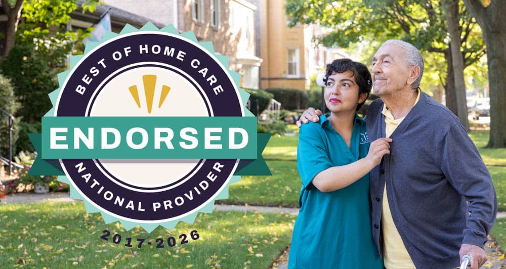 Female Right at Home caregiver helping a senior male client walk outside with a Best of Home Care Endorsed National Provider badge