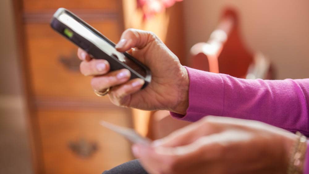 Woman holding a cell phone in one hand and a credit card in the other