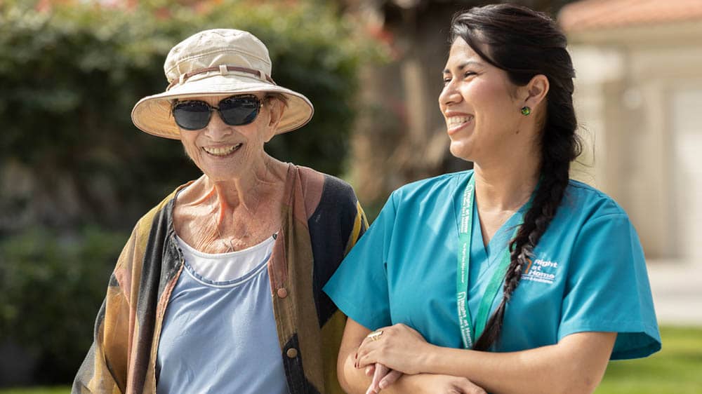 Senior female client outside walking arm in arm with female Right at Home caregiver